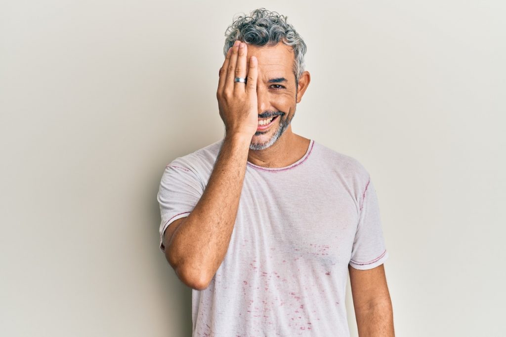 Uomo si copre un occhio mentre sorride. Deve fare l'intervento di maculopatia con luteina